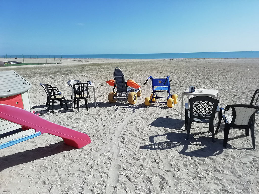 spiaggia lunga in sabbia con giochi per bambini e sedie per disabili