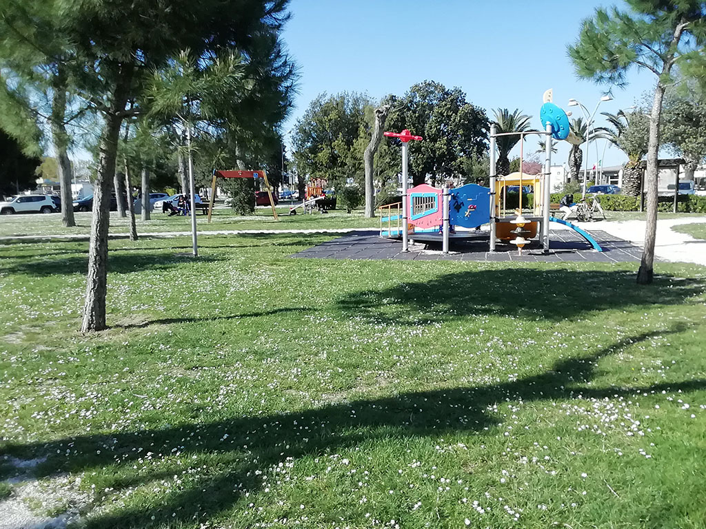 parco giochi in area con erba tra le case e con zone d'ombra sotto agli alberi