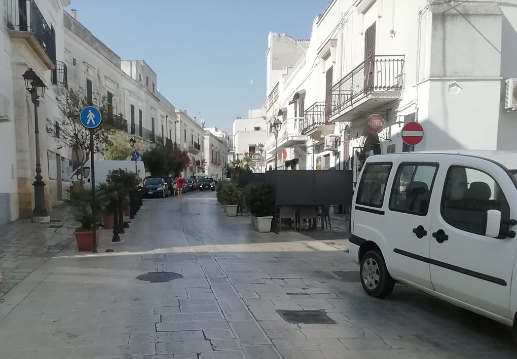 un'ampia strada lastricata e pianeggiante tra bassi palazzi con le facciate bianche. All'imbocco un segnale avvisa dell'inizio della zona pedonale.