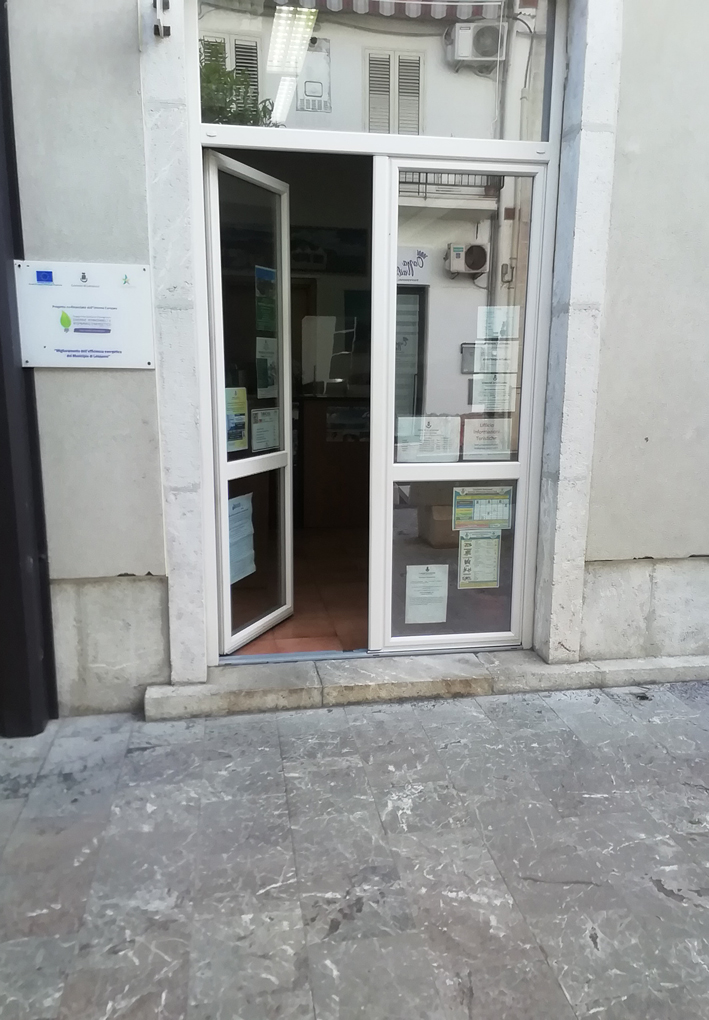 Accesso allo IAT. Una porta a vetri si apre verso l'interno della struttura. Presente un piccolo scalino in ingresso. 