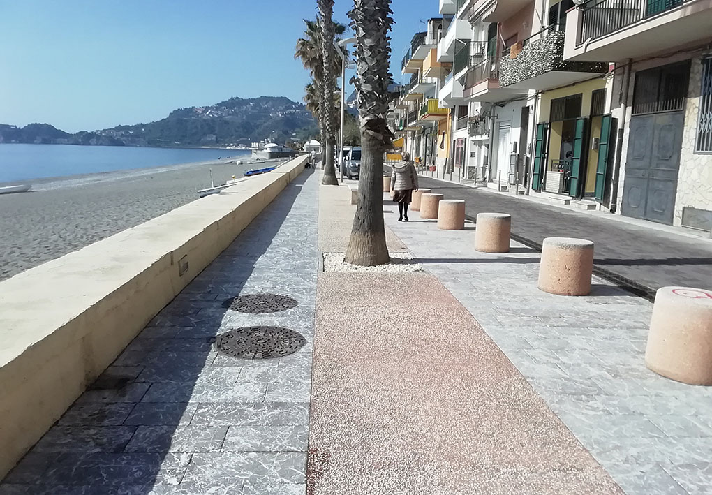 Passeggiata lungomare. Lungo il bordo del marciapiede corrono una serie di panettoni stradali di cemento, al centro sono piantate una fila di palme, che lasciano tuttavia sufficiente spazio per passare. Un muretto divide la passeggiata dalla spiaggia, dando anche la possibilita di sedercisi.