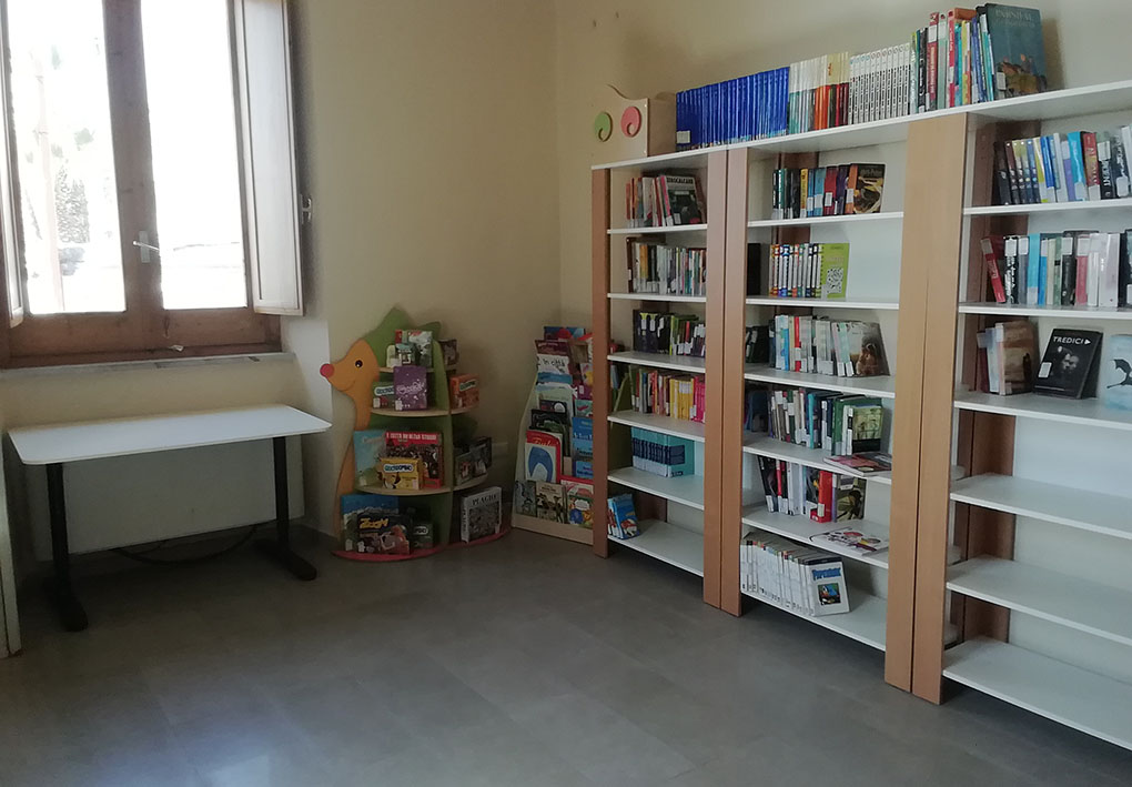 In una stanza luminosa, scaffali al muro, di cui uno a forma di porcospino, contengono libri per bambini. Sotto a una finestra è disponibile un tavolo da consultazione.