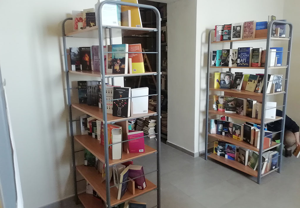 Scaffali a giorno  pieni di libri creano un corridoio in una stanza luminosa