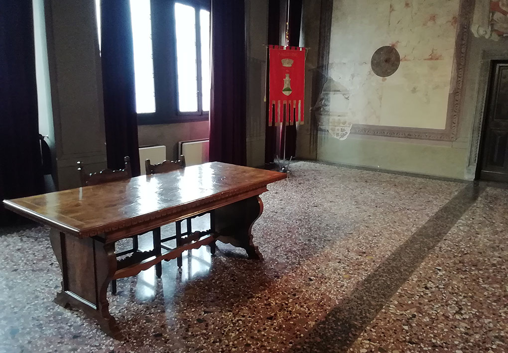 in una sala di un palazzo storico, si vede un tavolo antico e il gonfalone del comune