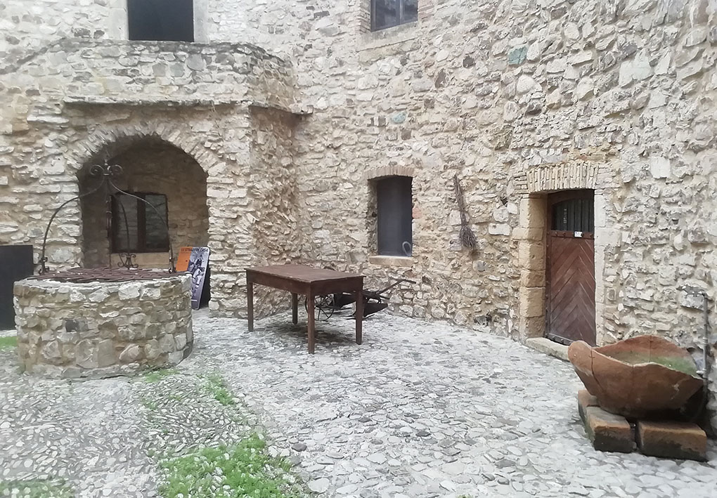 cortile interno di una antica costruzione in pietra. si notano arredi storici in esposizione e, al centro, un pozzo.