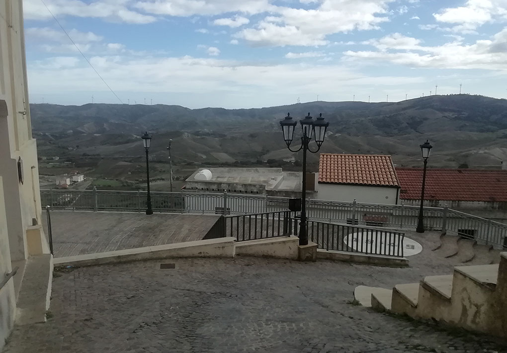 Dalla cima di una ripida discesa che finisce in un piazzale protetto da una ringhiera, si apre il panorama sui tetti degli edifici sottostanti di Melissa e che si estende fino alle colline di fronte.