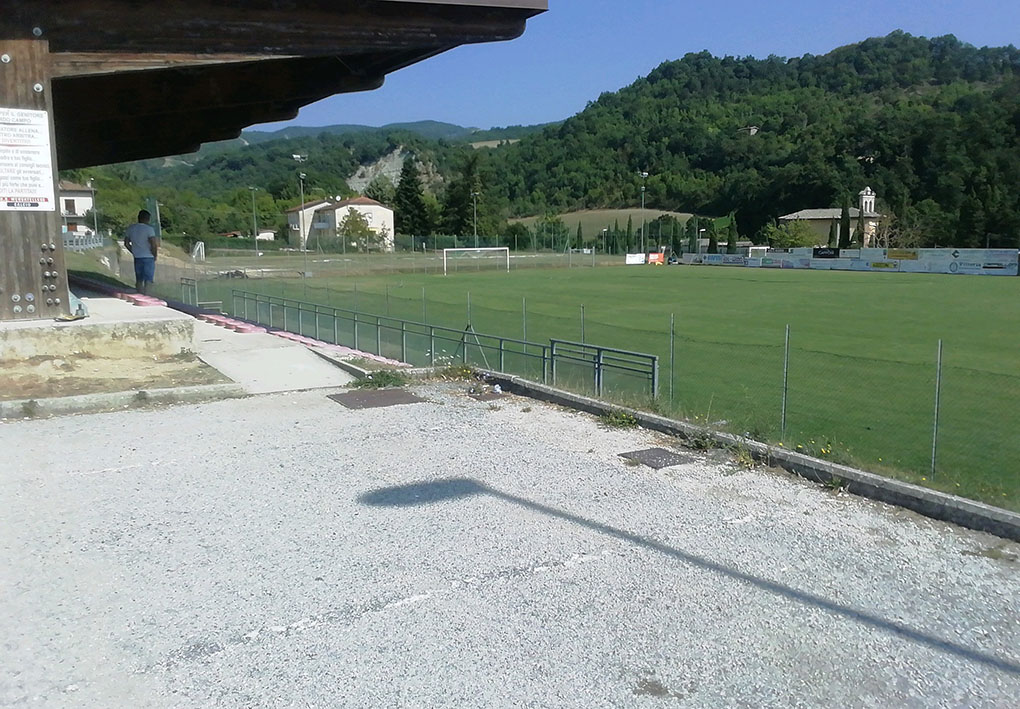 Campo da gioco in erba, visto dagli spalti, coperti da una tettoia.