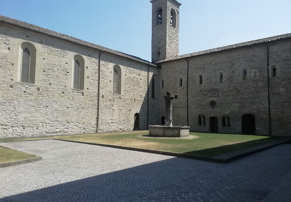 Chiostro interno di un convento storico. Le facciate di pietra presentano piccole finestre secondo l'uso dell'epoca. Al centro, in un'aiuola curata, sorge una statua.