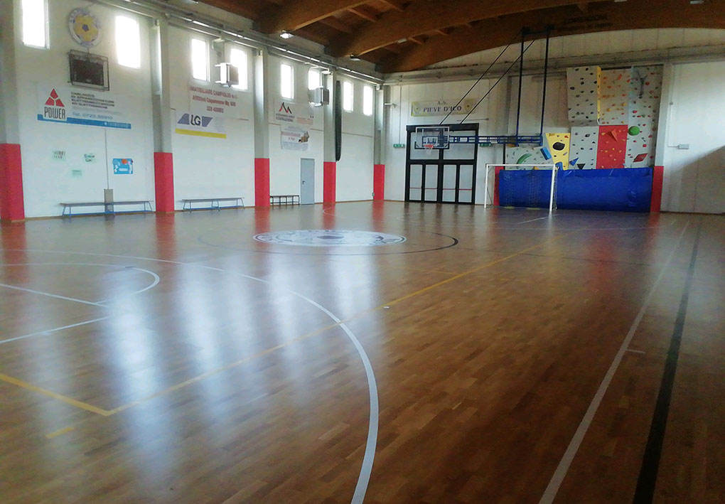 Campo sportivo indoor con pavimento in parquet e copertura in legno. Le finestre in alto illuminano l'ambiente.