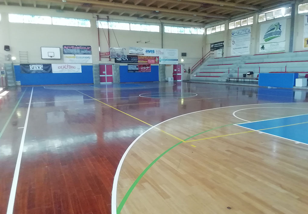 Campo sportivo in parquet, sul fondo sono montati canestri. Sul lato spalti a gradoni.