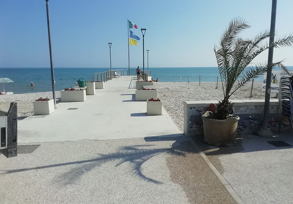 un molo in cemento si allunga verso il mare. Ai suoi lati continua la spiaggia