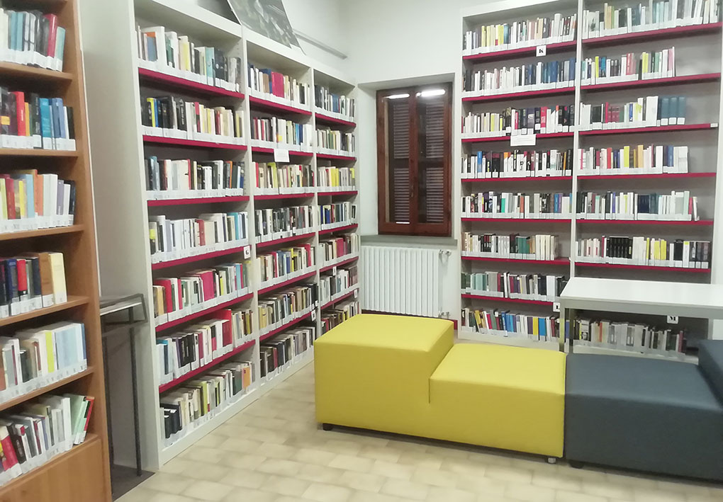 Una sala della biblioteca, con un divanetto centrale e fitti scaffali di libri alle pareti.