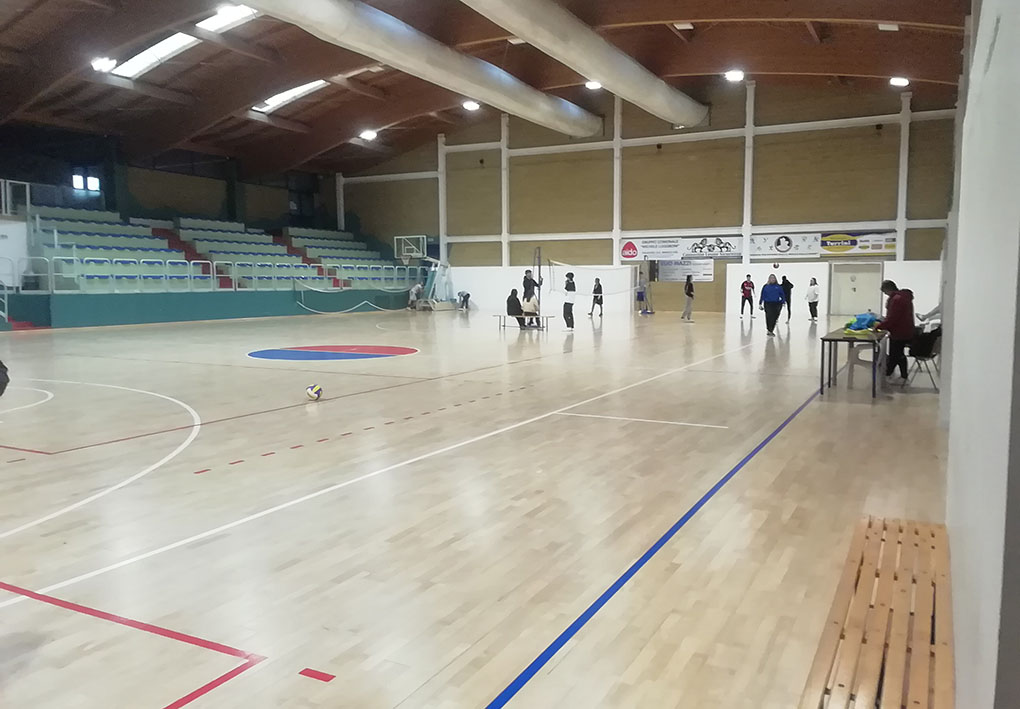 Interno di un moderno palasport ben illuminato. Su un lato della costruzione sorgono gli spalti. AL centro del campo ragazzini fanno attività fisica