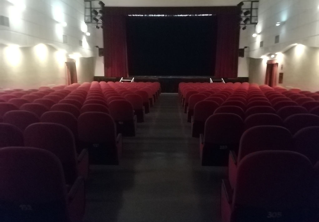 Sala interna del cinema, con numerose file di poltroncine in velluto. Un corridoio centrale percorre la platea.