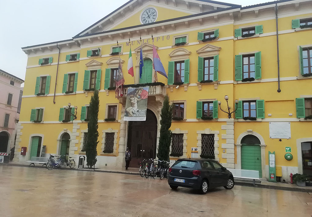 Il palazzo storico che ospita il Comune si affaccia sulla piazza principale con un grosso portone. AI lati di questo, due piante in vaso decorano l'ingresso. Poco distante è posteggiata un'auto che ha potuto accedere alla piazza pedonale