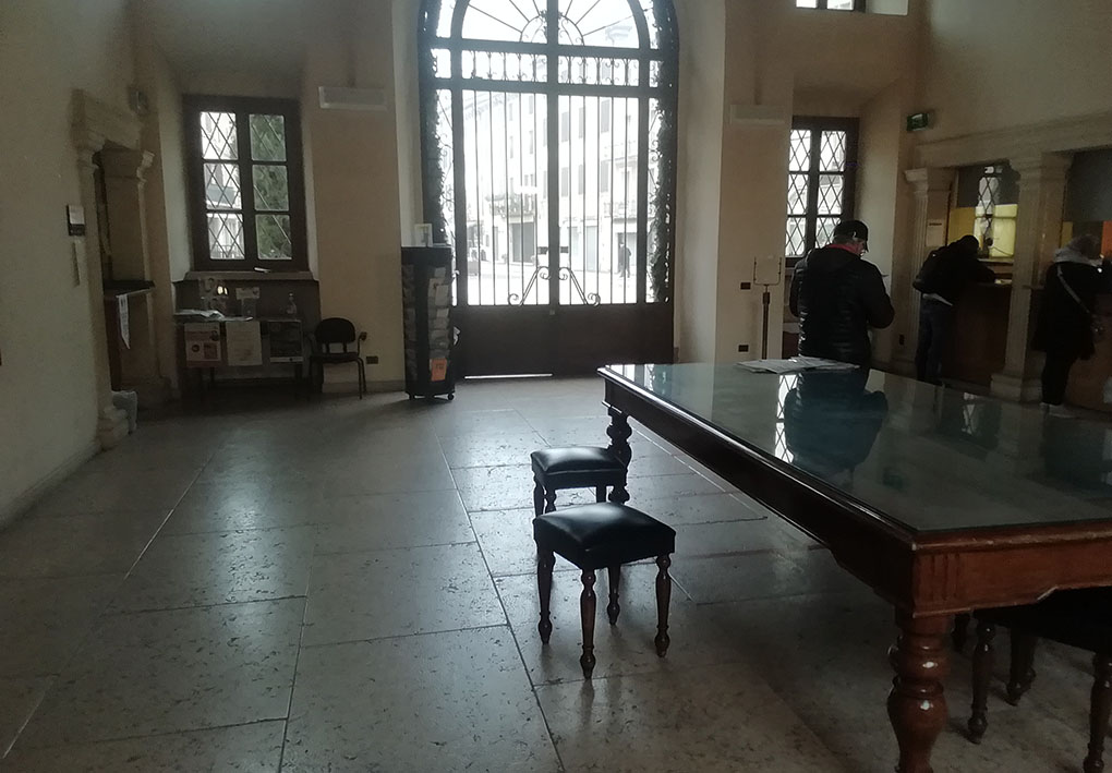 Interno dell'ingresso del palazzo comunale. Un portone si affaccia verso l'esterno, mentre al centro della stanza è posto un tavolo ottocentesco