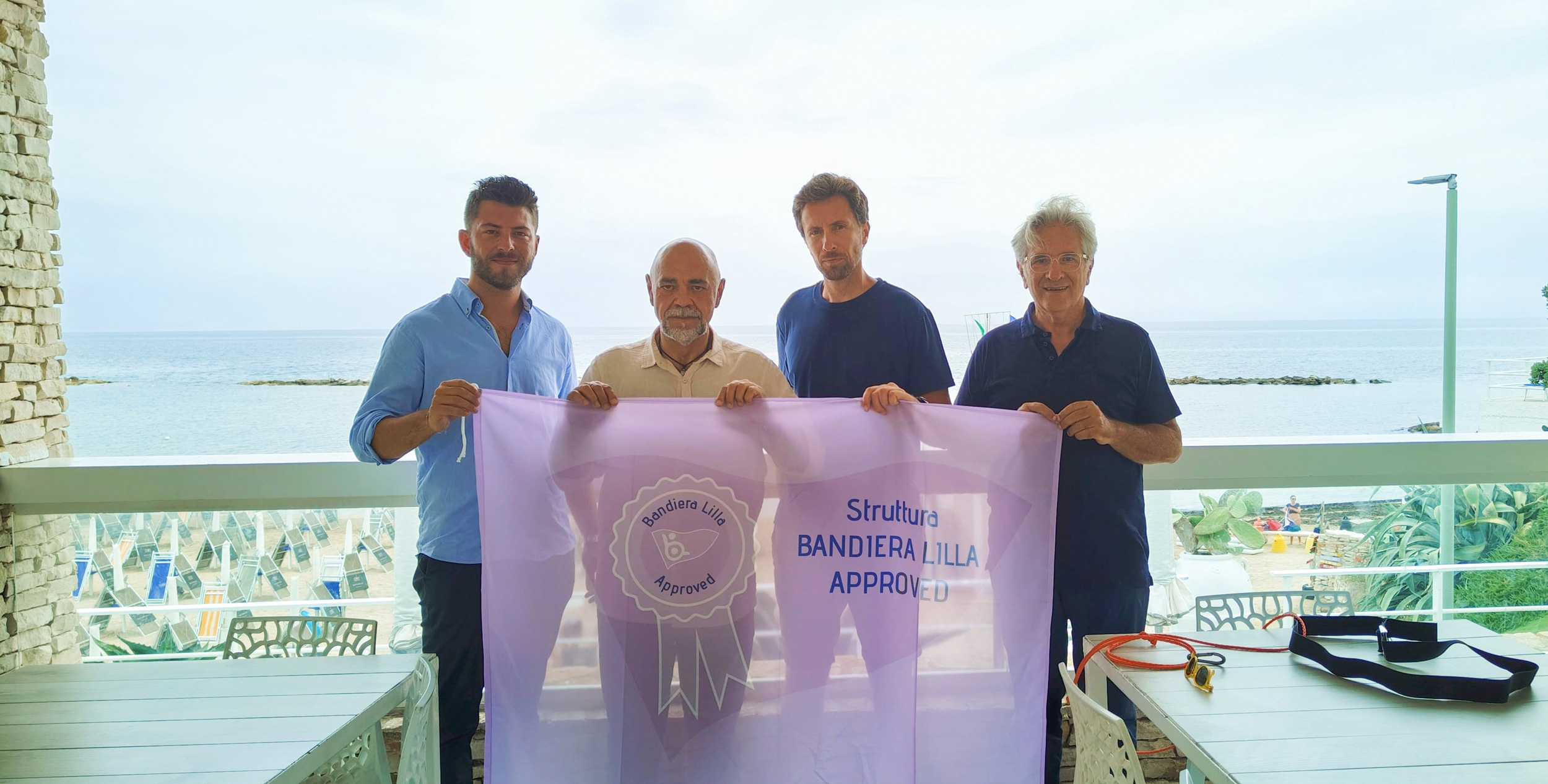 Il presidente e il direttore di Bandiera Lilla posano con i gestori della struttura. Sullo fondo la spiaggia